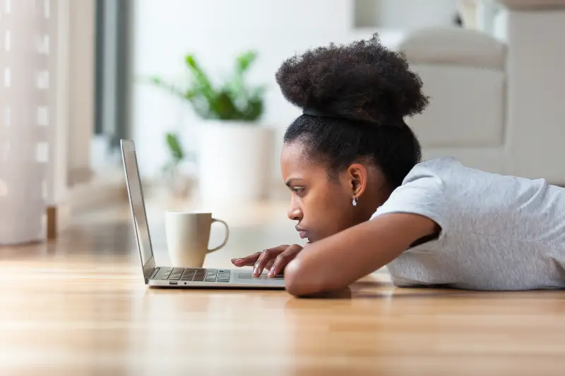 allvarligt fokuserad ung svart kvinna på golvet med sin bärbara dator