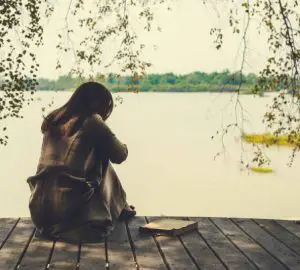 ensam tjej som sitter på trä vid sjön