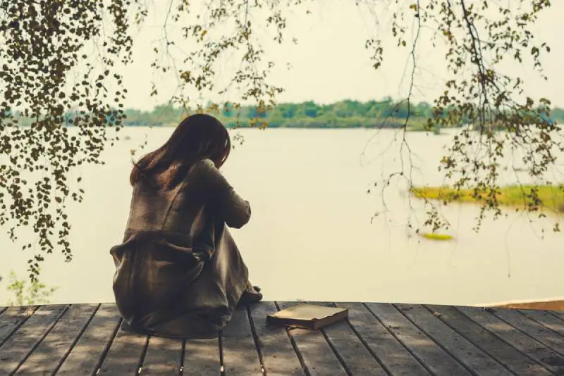 ensam tjej som sitter på trä vid sjön