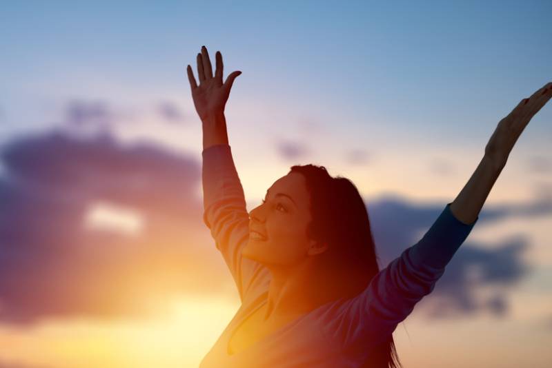 glad kvinna med händerna upp vid solnedgången