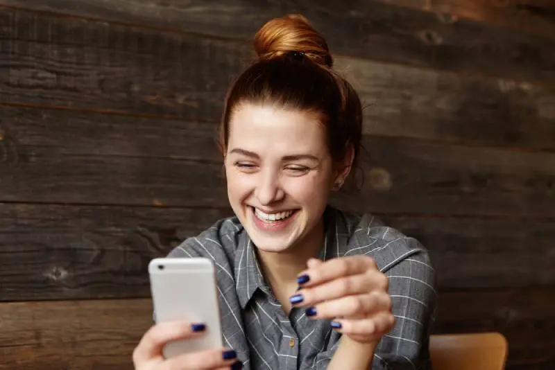 leende flicka tittar på sin telefon på caféet